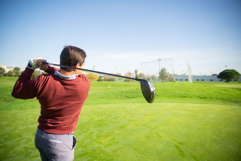 A golfer in a red sweater swings on a sunny day in Portugal's green golf course.