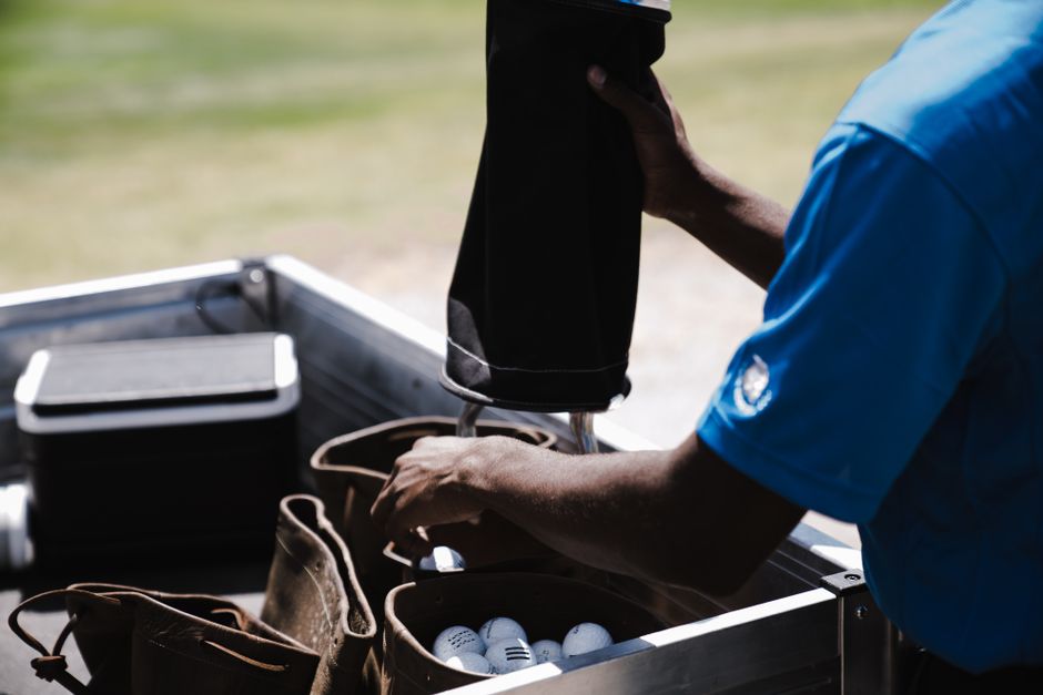 A man in a blue shirt organizing golf balls and leather bags outdoors on a sunny day.