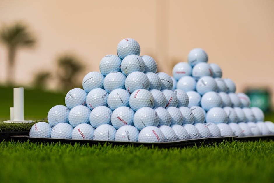 Close-up image of golf balls stacked in a pyramid shape on the grass outdoors.