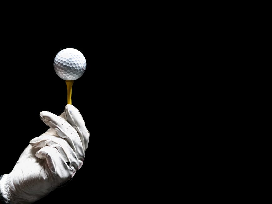 Close-up of a golf ball on a tee held by a gloved hand on a black background.