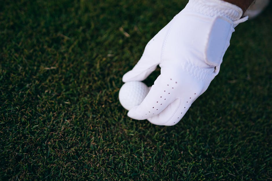 Close-up of a golfer's hand in a glove placing a golf ball on a green field.