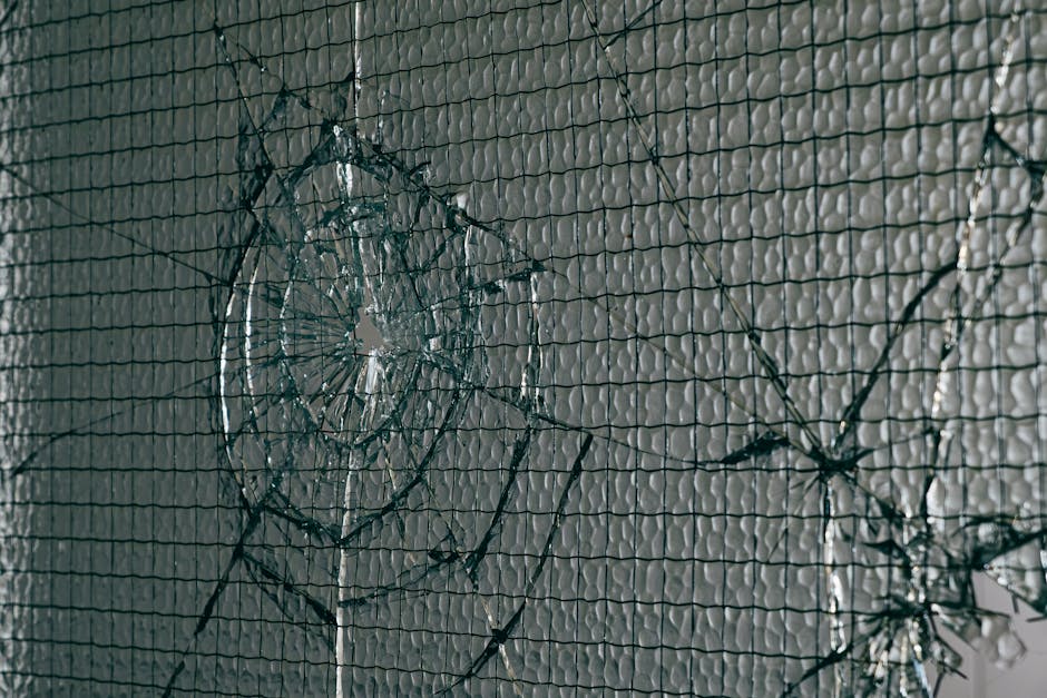 Close-up view of a shattered safety glass window with intricate wire patterns and light reflections.