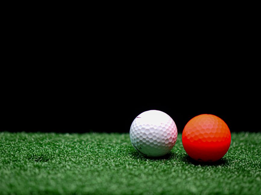 Close-up view of white and orange golf balls on artificial grass with a dark background.