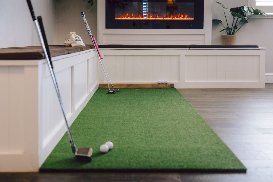 Cozy indoor putting green setup with golf clubs and a warm fireplace, perfect for practice.