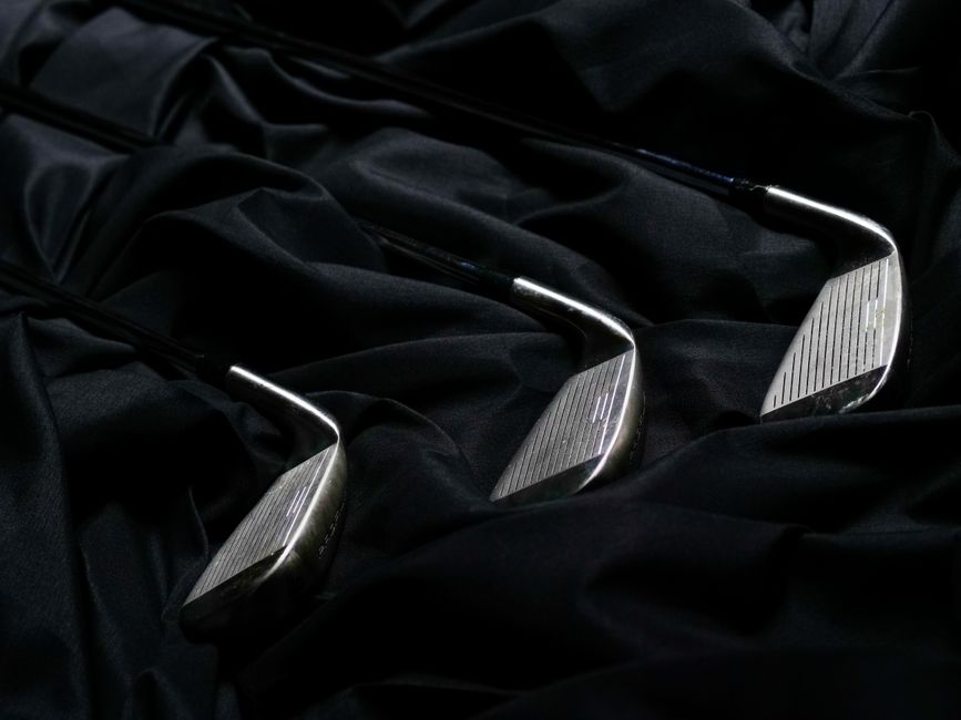 Elegant close-up of metal golf clubs placed on creased black fabric, ideal for sports equipment themes.