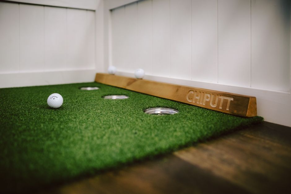 Indoor putting green with golf balls and training aid for golf practice.