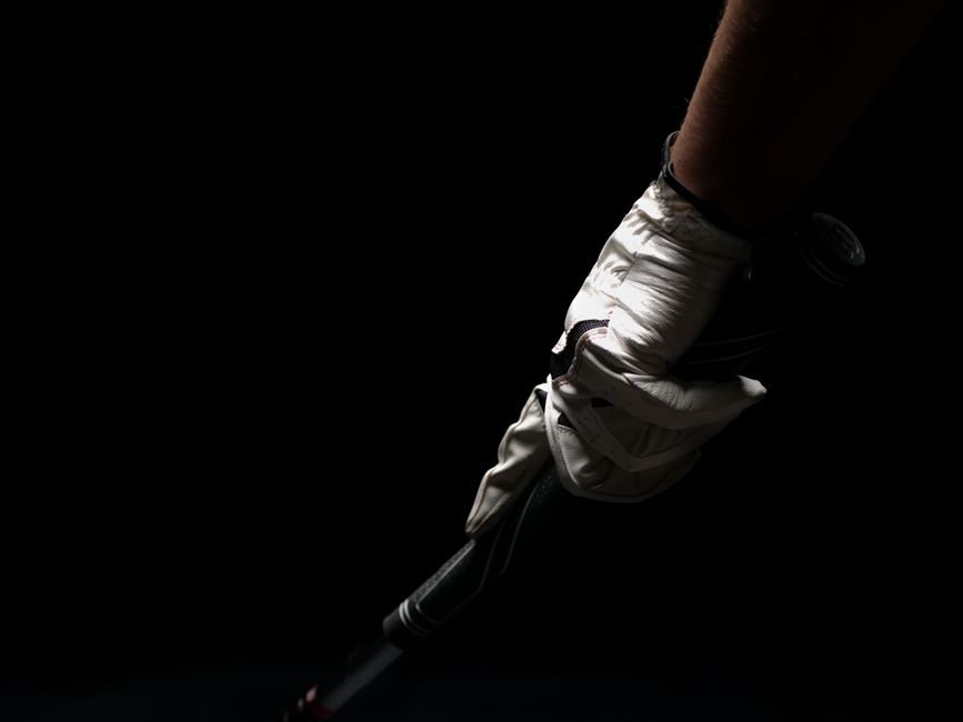 A close-up shot of a golfer's hand in a white glove gripping a golf club against a black background.