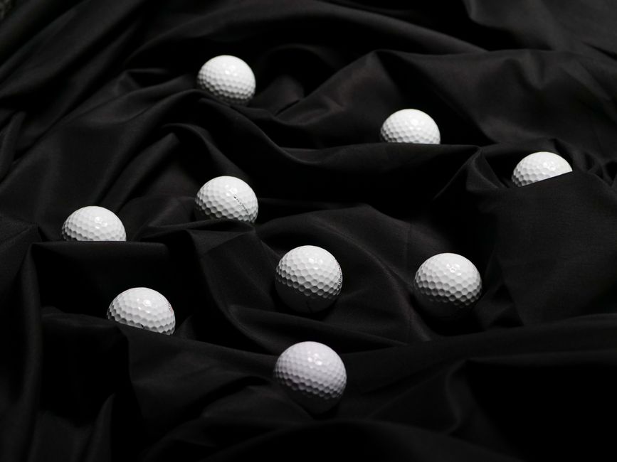 Close-up of white golf balls scattered on smooth black fabric.