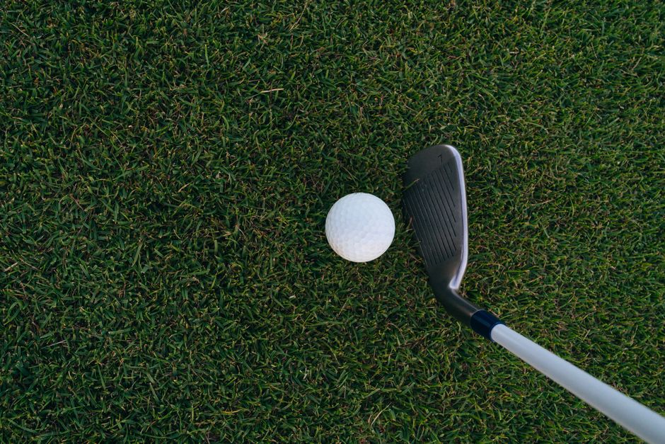 Detailed shot of a golf club aligning with a ball on a lush green grassy surface.